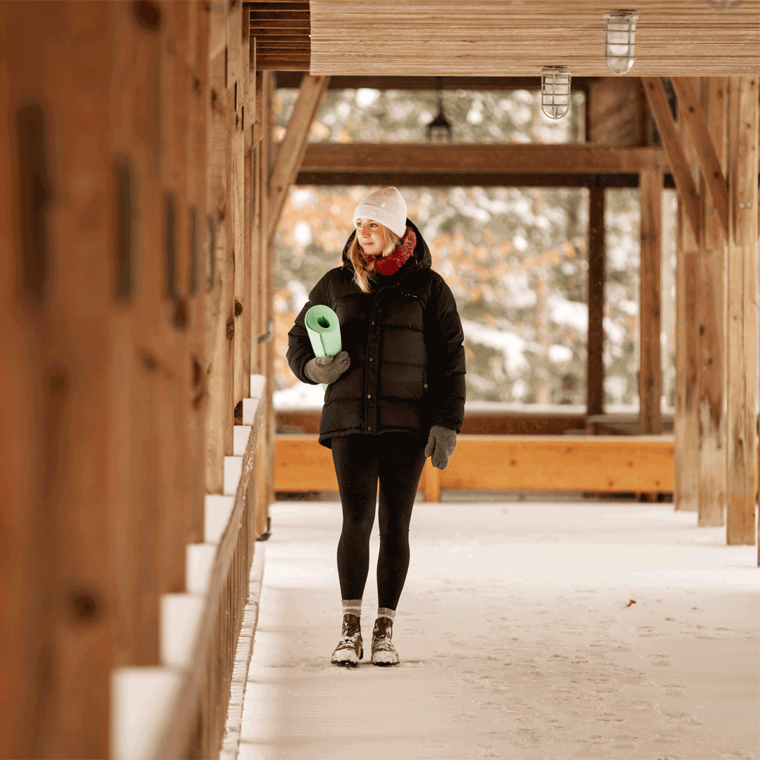 Woman walking on winter pathway with yoga mat
