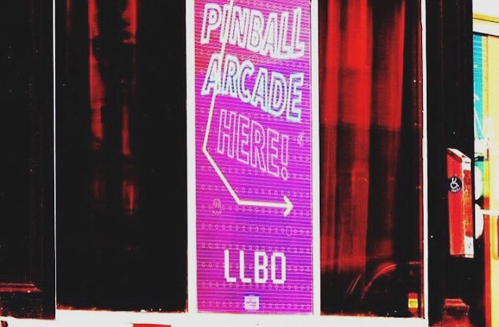 Window sign at last level lounge barrie featuring pink sign saying "pinball arcade here"