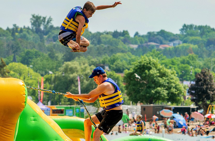 Kid jumping from platform at Splash ON Water park with dad climbing the rope