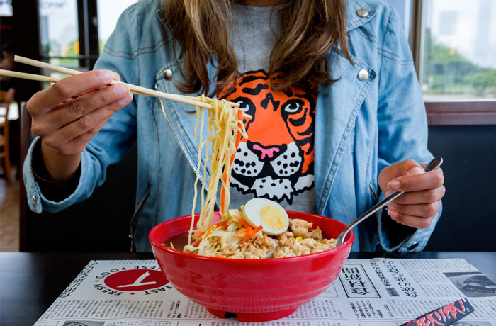 A woman with a tiger shirt eating a bowl of noodles from Teriyaki Experience