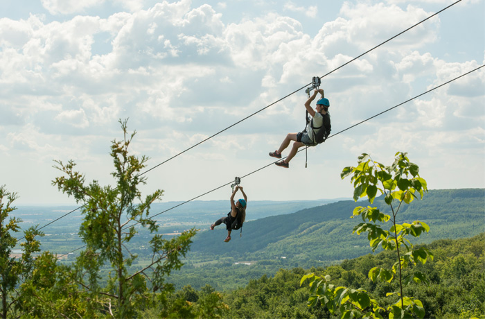 Two people zip lining side by side above the trees at Scenic Caves Thunderbird Zip line